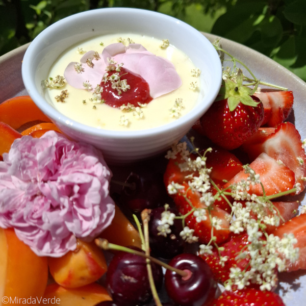 Holunderblütenpudding mit Rosen- und Holunderblüten und Erdbeermus garniert. Am Obstteller