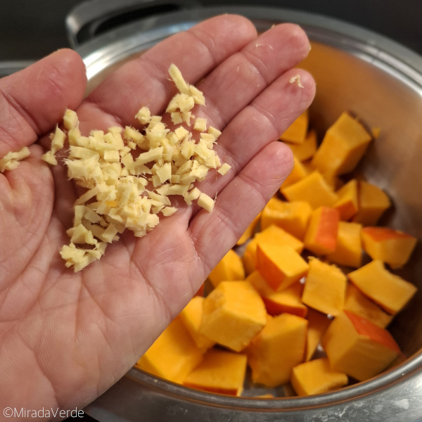 Gehackter Ingwer in der Hand. Hokkaido Kürbis im Kochtopf